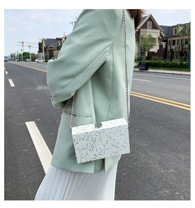Detail of white box clutch bag with colorful speckles and silver chain strap in street view