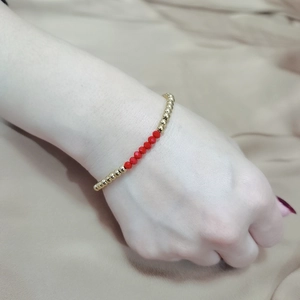 Detail view of gold bead bracelet with red faceted crystals on model wrist