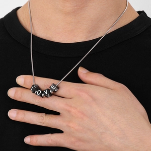 Detail of silver snake chain necklace with black cubes spelling LOVE on model neck