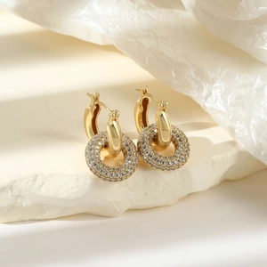 Elegant gold double hoop earrings with paved white zircons on a white stone background
