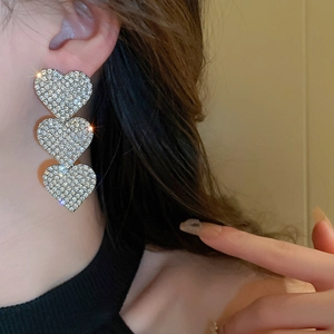 Macro detail of silver-tone triple heart drop earrings with shimmering pavé rhinestones