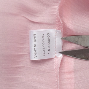 Detailed macro shot of the 100% polyester fabric care label on a pink chiffon dress