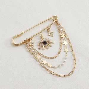 Detail of gold evil eye brooch with layered chains, pearls and star charms on white fabric