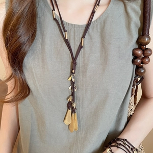 Detail of long bohemian necklace featuring golden metal leaves and brown woven rope