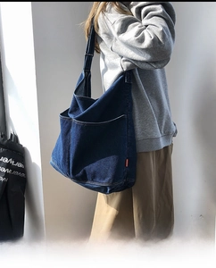 Detail of dark blue denim crossbody bag with dual front pockets and adjustable strap
