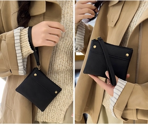 Close-up of a black minimalist leather coin purse with wristlet strap and gold rivets