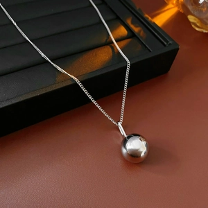 Detailed view of polished silver metal sphere pendant on a minimalist chain