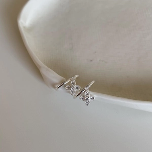 Detailed view of silver clover earrings with white zircon on ceramic dish edge