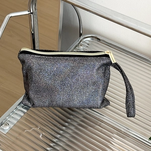 Detailed close-up of a black glitter makeup bag with gold zipper on a glass shelf