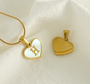 Detailed close-up of heart-shaped gold necklace with shell inlay and letter H