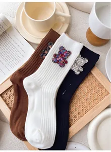 Detailed view of knitted mid-calf socks with rhinestone bear motifs in white, brown and black
