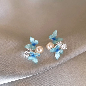 Close-up of sparkling blue butterfly earrings with white pearls and zirconia accents