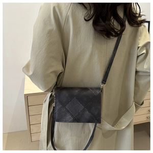 Detail view of black quilted crossbody bag with golden buckle on a trench coat