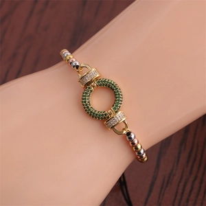 Makroaufnahme des dreifarbigen Perlenarmbands mit grünem Zirkonring auf Holzgrund