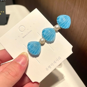 Detailed close-up of blue shell and white pearl hair clip on a paper display card