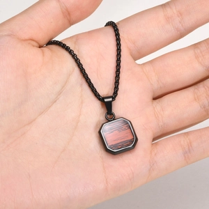 Detail of square stainless steel necklace with tiger eye stone held in hand