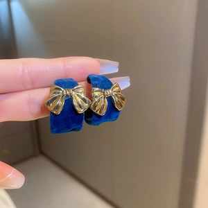 Detail view of dark blue velvet C-shaped hoop earrings with a gold metal bow ornament
