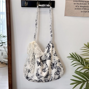 Detailed macro of white fabric tote bag featuring black butterfly prints and lace bow ribbon
