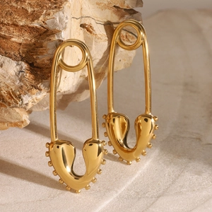 Golden heart-shaped safety pin earrings on a natural stone background with luxury lighting