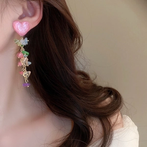 Détail de pampilles en pierres colorées et boucle d'oreille cœur rose sur un modèle