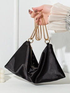 Minimalist black satin tote bag with gold metal chain shown in hand against white background