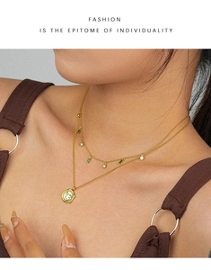Detail of a layered gold necklace featuring a green rectangle gem and a rabbit pendant