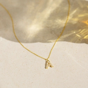 Macro shot of gold letter A pendant with inlaid pearls on a delicate chain necklace