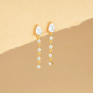 Detail of gold dangle earrings with drop-shaped white gemstones and a polished finish