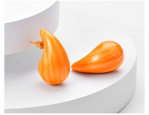 Detailed macro view of orange teardrop earrings with pearlescent sand texture