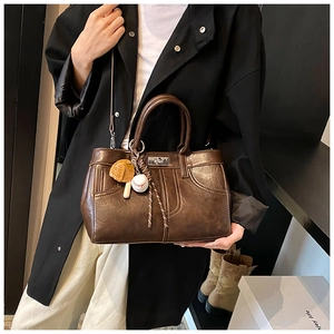 Détail du sac en cuir marron vintage avec fermoir rotatif argenté et charm de baseball