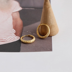 Close-up of golden hoop earrings with sandy glitter texture on a minimalist wooden stand