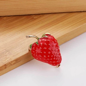 Creative strawberry brooch with red and green enamel coating on natural wood surface
