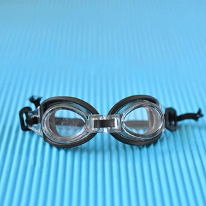 Gros plan de lunettes de natation miniatures pour poupées avec montures noires et verres.