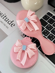 Detailansicht von rosa Haarbürste mit Schleife und passendem Taschenspiegel auf Laptop