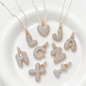Gold plated bubble letter and heart pendants with cubic zirconia inlay on white tray