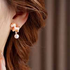 Close-up of pink and gold unicorn earrings with hanging pearl on model's ear