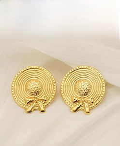 Detail of golden stainless steel bowknot straw hat earrings on elegant white silk background
