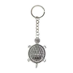 Detail of silver vintage turtle keychain with intricate patterns on a white background