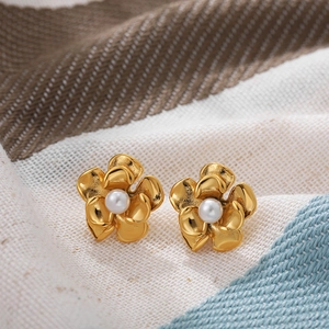 Close-up of 18k gold flower earrings featuring a pearl center on soft fabric background