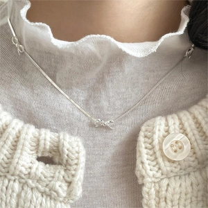 Close-up of a silver bow-knot snake chain necklace on model with knit cardigan