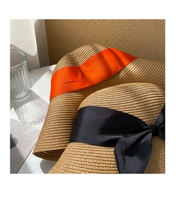 Detail of woven straw sun hat featuring elegant orange ribbon and black bow accents