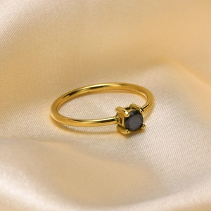 Detail of gold titanium ring with a black round gemstone on champagne silk fabric