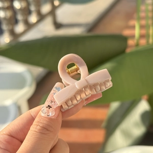 Close-up of a mini pink bow hair claw clip with golden metal spring in natural light