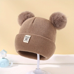 Dettaglio del cappello in maglia marrone per neonati con due pompon e etichetta morbida