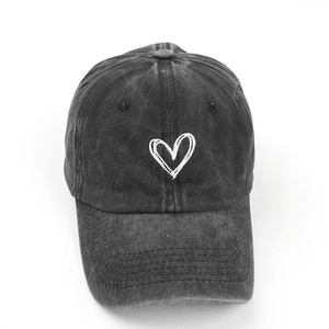Close-up of a washed black cotton baseball cap with white embroidered heart detail