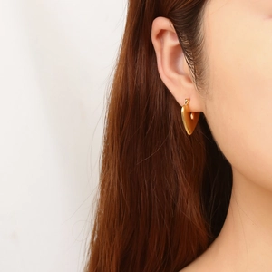 Close-up of golden heart-shaped earrings with mirror-polished finish on model