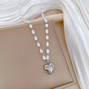Detailed shot of a beaded pearl necklace with a 3D silver heart pendant on silk