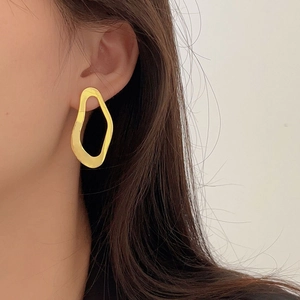 Close-up of irregular hollow oval gold earring worn by a model in a minimalist style