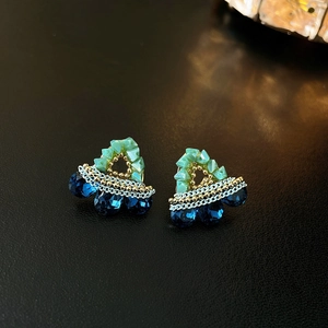 Detailed view of handmade triangle earrings with blue and green beads on a leather surface