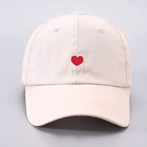 Close-up of a small red heart embroidery on the front of a beige canvas baseball cap